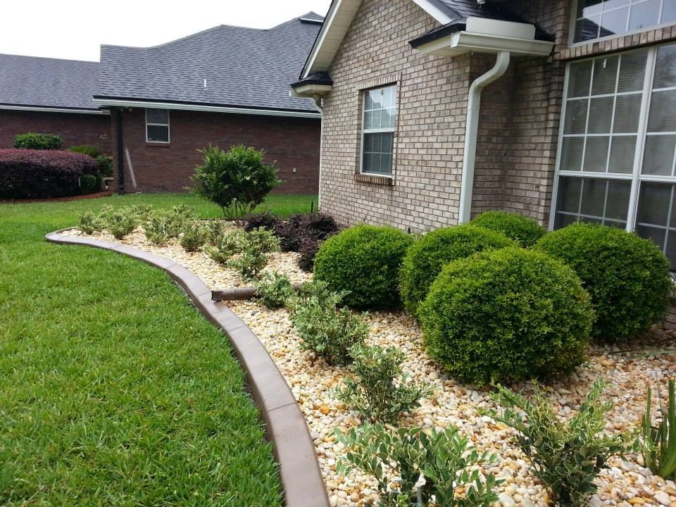 Curved flower bed with shrubs along a brick house beside a green lawn
