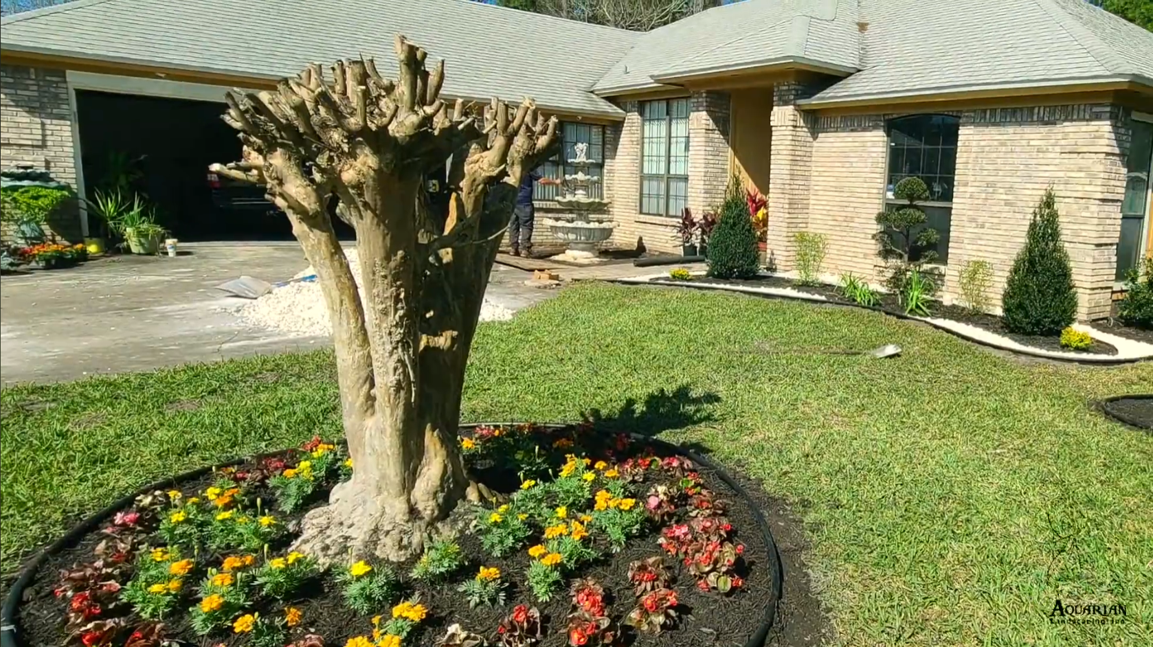 Landscaped front yard with a pruned tree, colorful flower bed, and stone house exterior