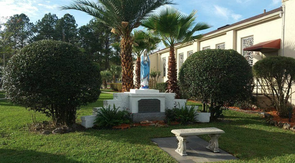 Landscaped courtyard with trimmed trees, white bench, and a small monument under palm trees