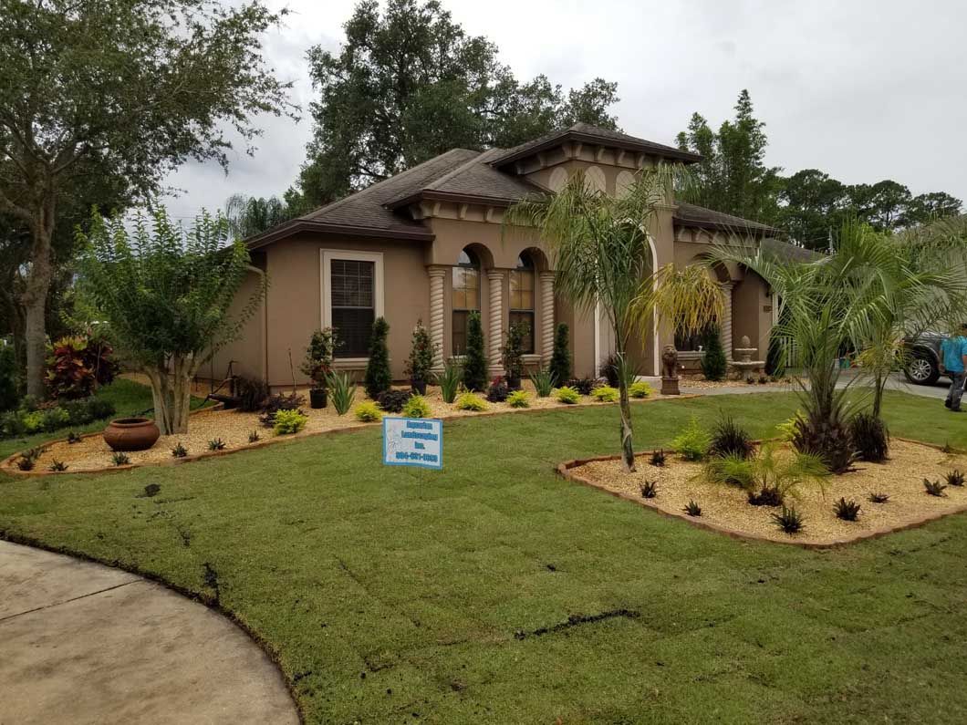 Suburban house with manicured lawn, landscaped front yard, and a small sign near the walkway