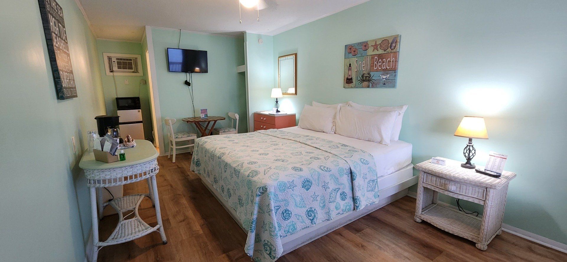 A bedroom with light green walls, a white wicker vanity and nightstand, and a bed featuring a blue and white quilt.