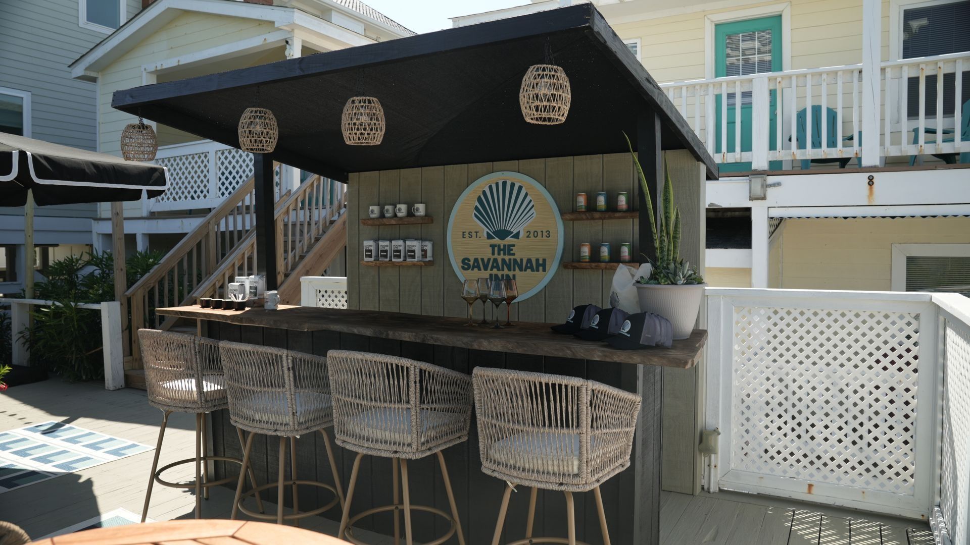 An outdoor bar with four woven bar stools, a black roof, and a circular sign reading 