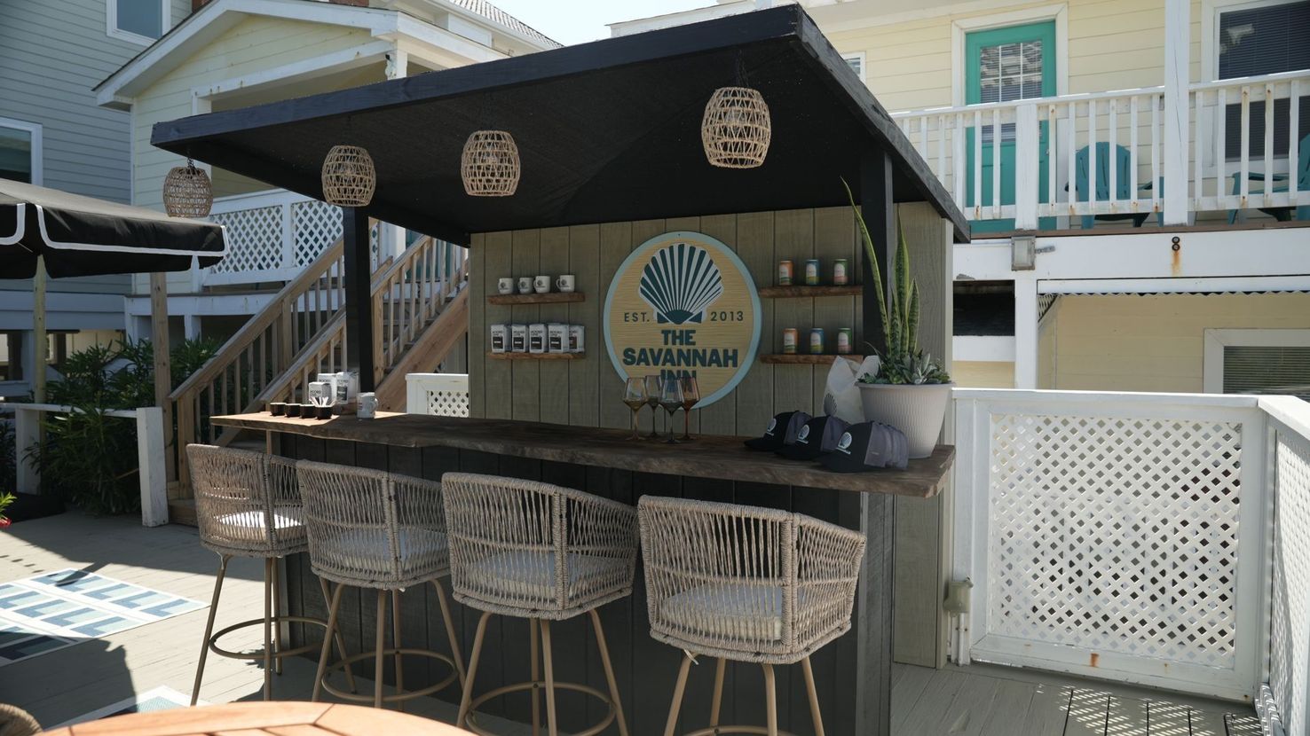 An outdoor bar with four woven bar stools, a black roof, and a circular sign reading 