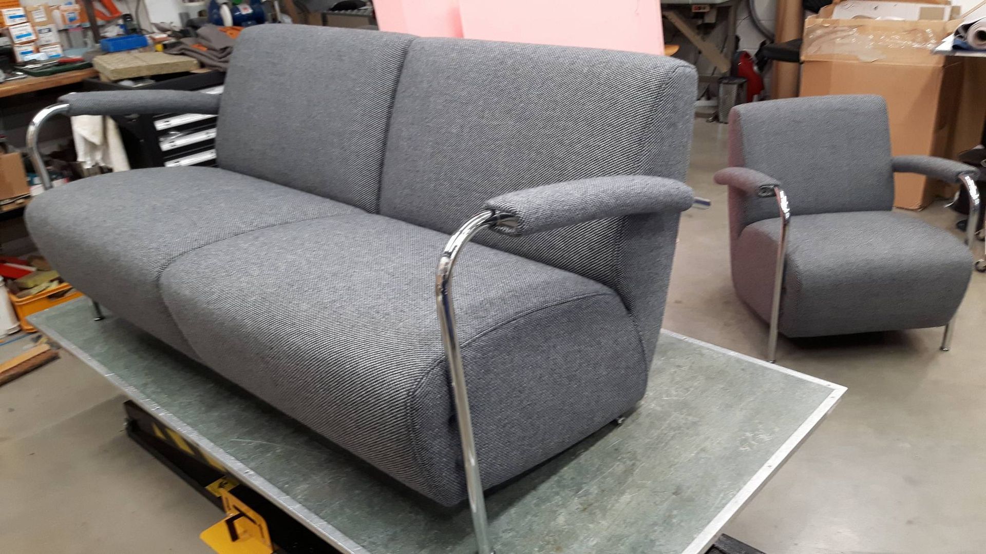 Grijze bank met patroon en bijpassende fauteuil op een werktafel in een werkplaats of stoffeerderij