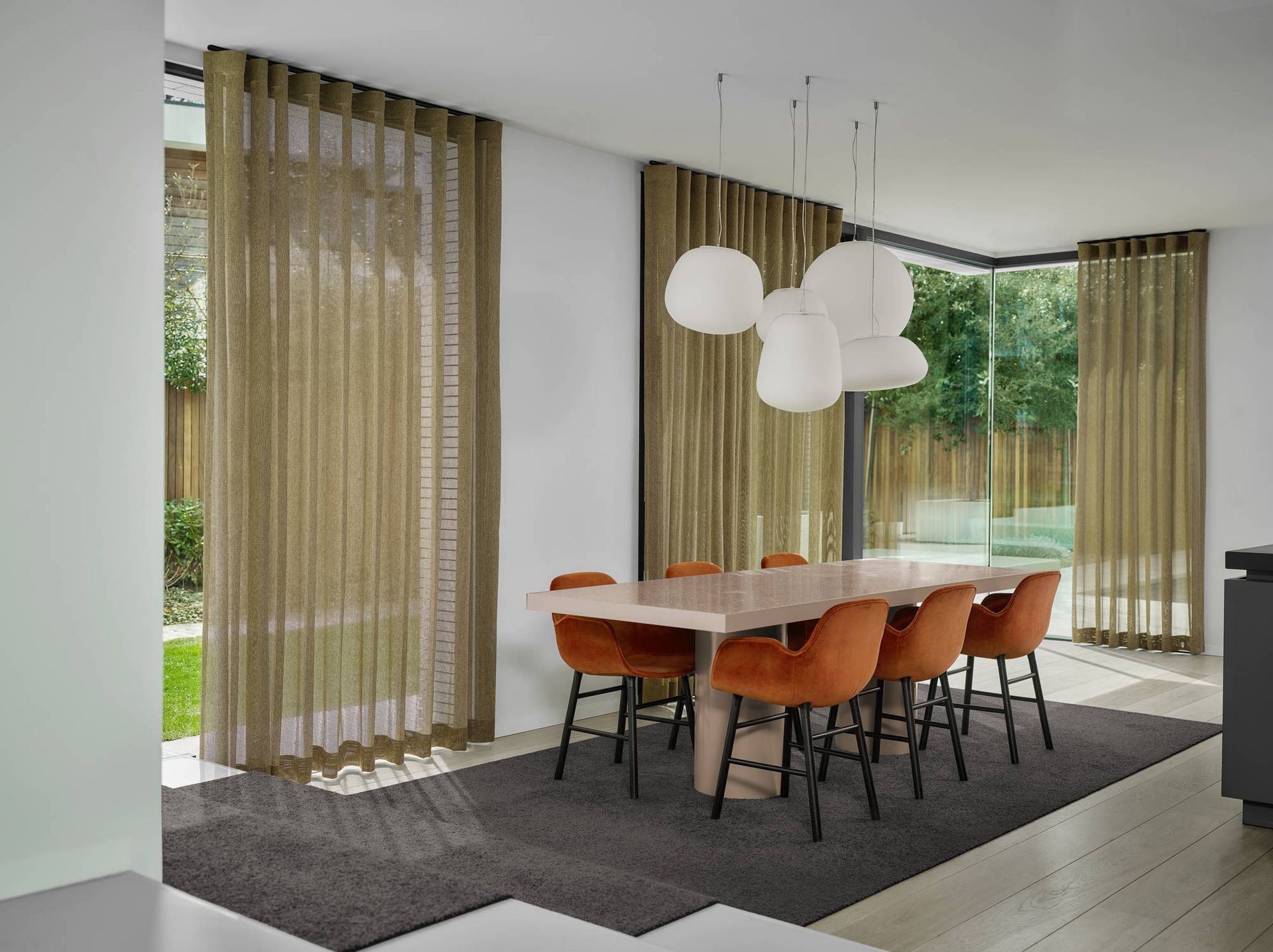 Moderne eetkamer met oranje stoelen, hanglampen en grote ramen met vitrage