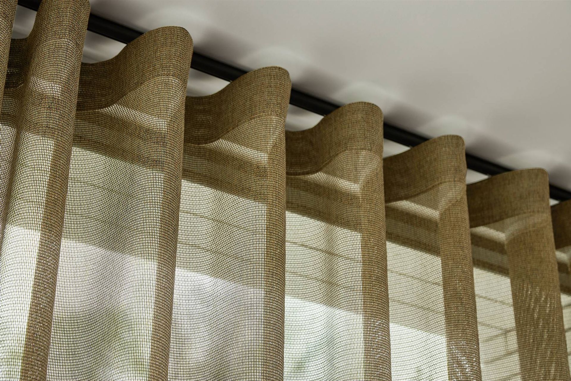 Beige transparante gordijnen die in zachte plooien voor een raam hangen, verlicht door daglicht