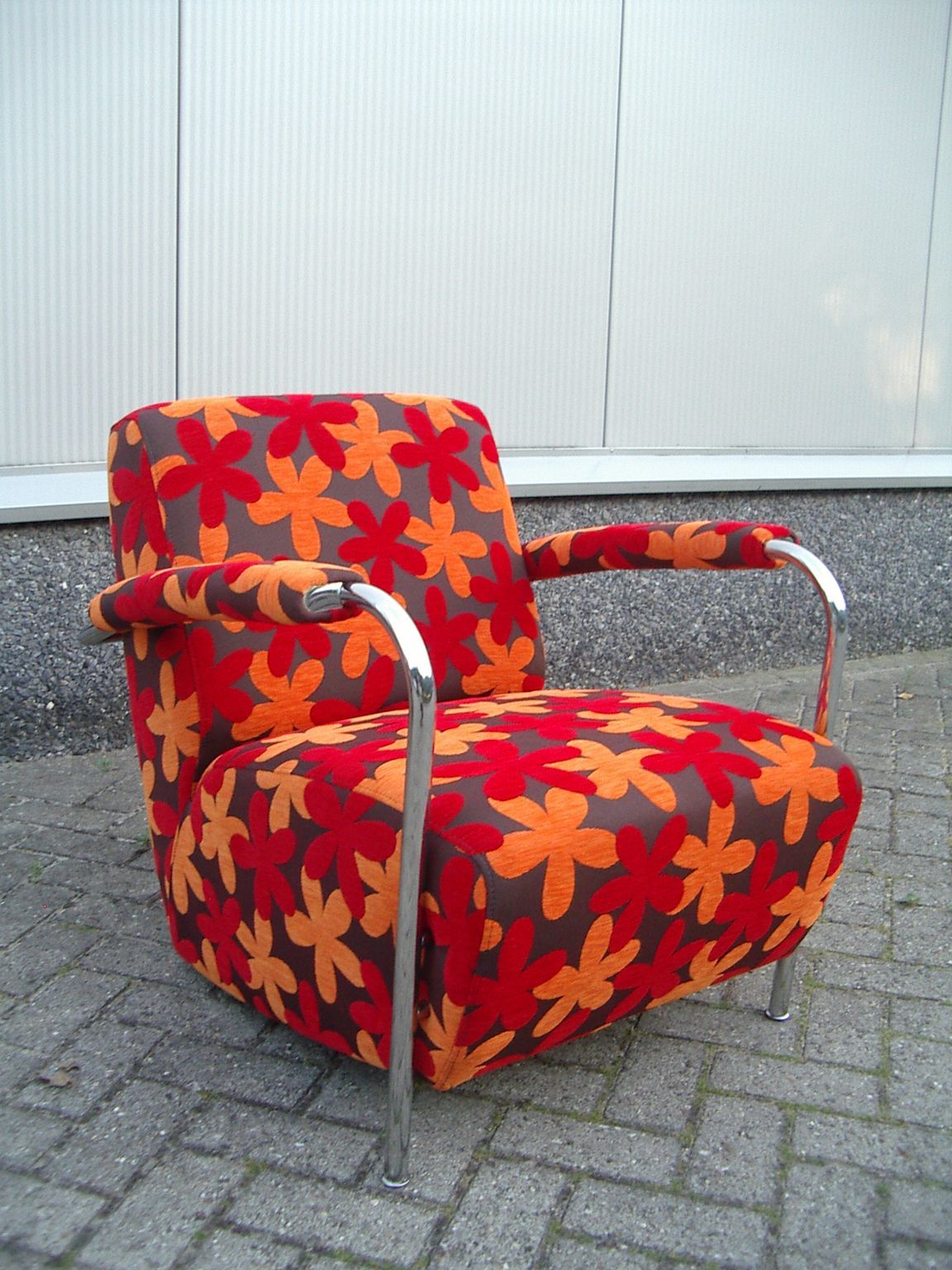 Kleurrijke fauteuil met bloemenprint, metalen armleuningen en bekleding, op een stenen bestrating