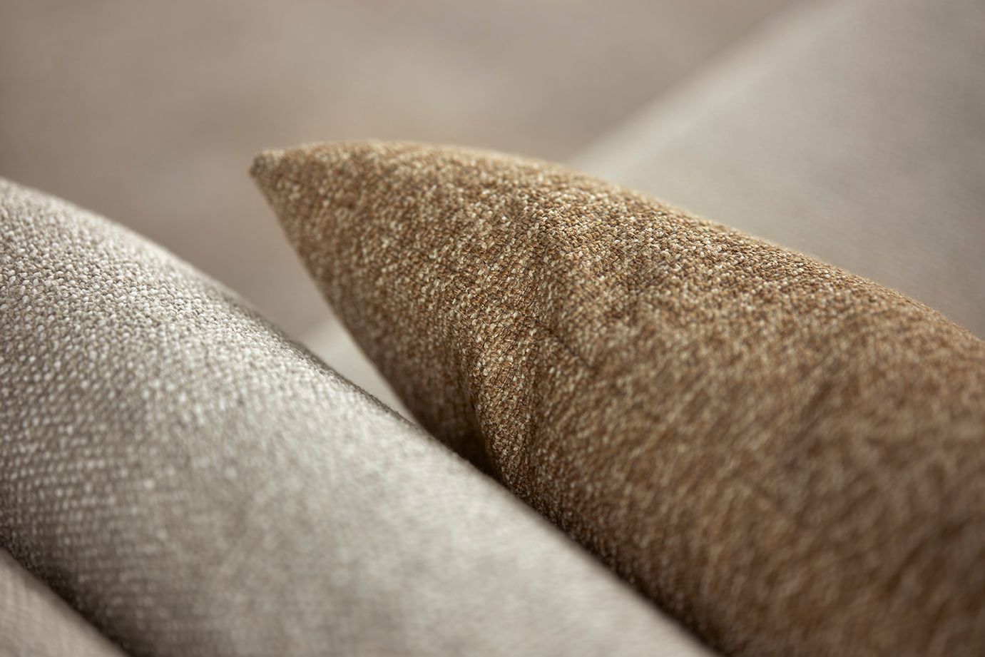 Close-up van twee kussens van gestructureerde stof in beige- en bruintinten.