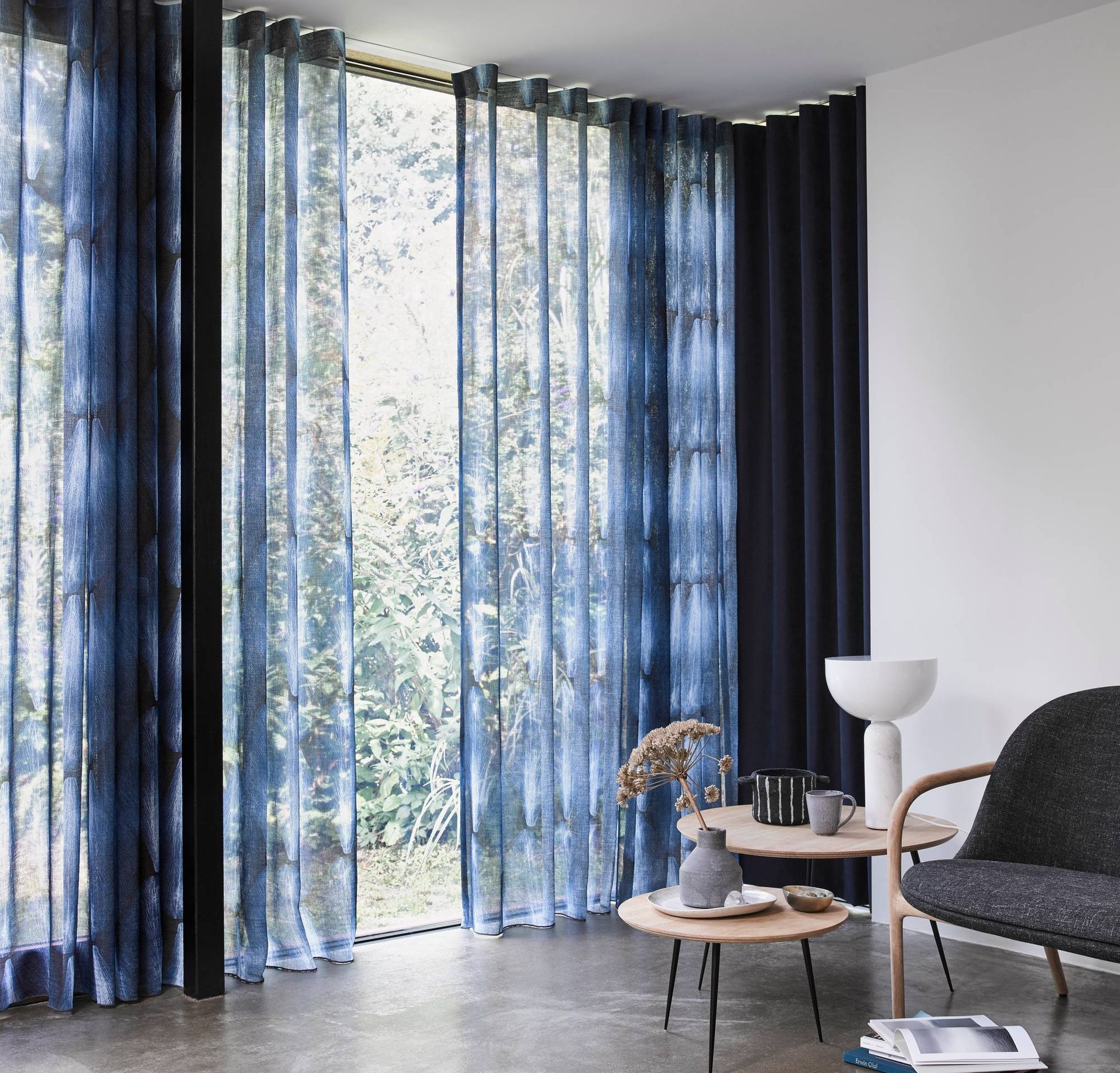 Moderne woonkamer met blauwe vitrages van vloer tot plafond, fauteuils en een kleine salontafel