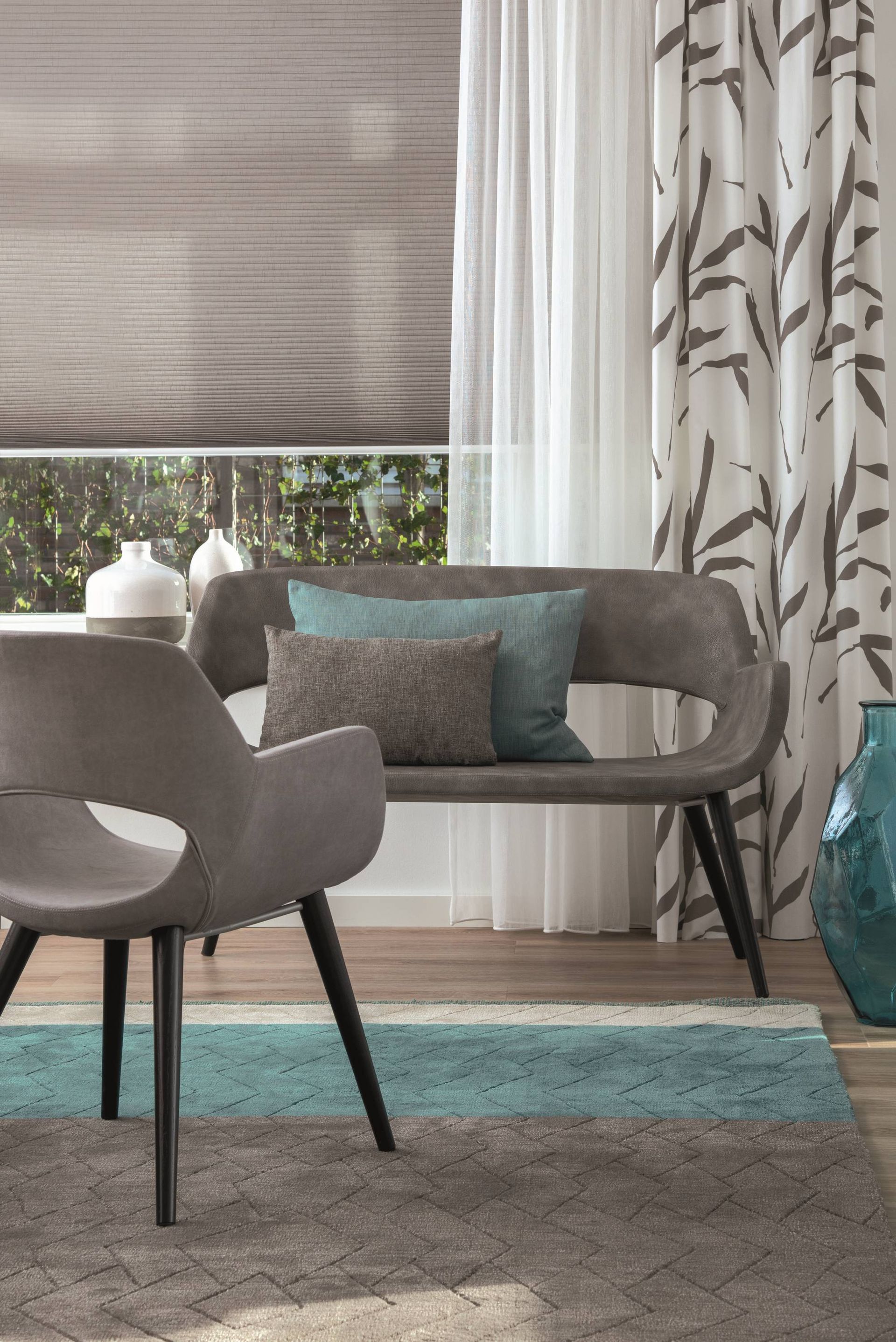 Moderne woonkamer met grijze stoelen, een turquoise vloerkleed, vitrage en gedessineerde gordijnen bij een raam