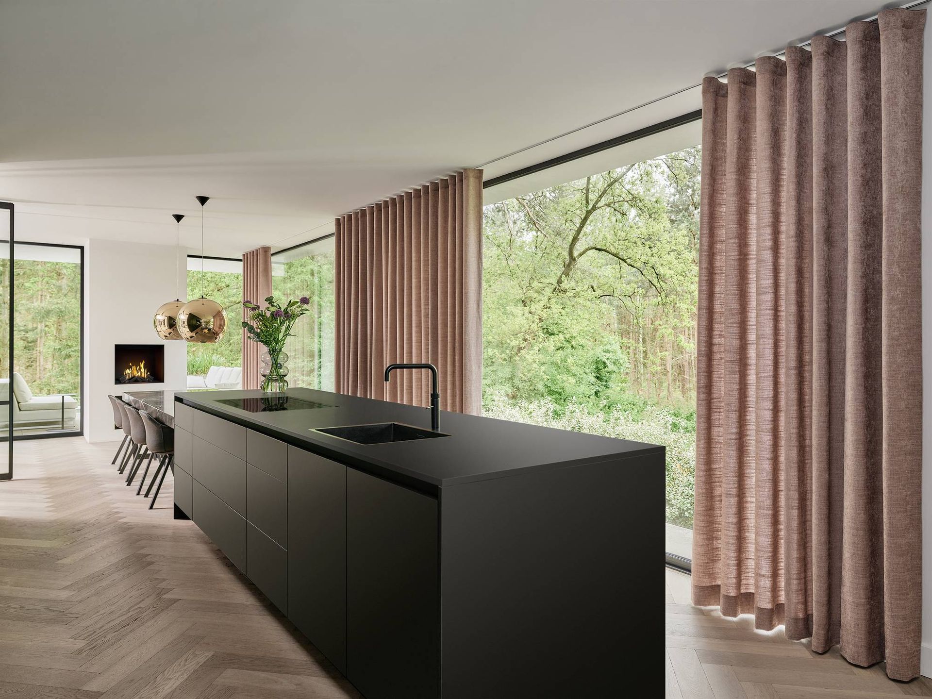 Moderne keuken met een matzwart kookeiland, roze gordijnen en grote ramen met uitzicht op het groen