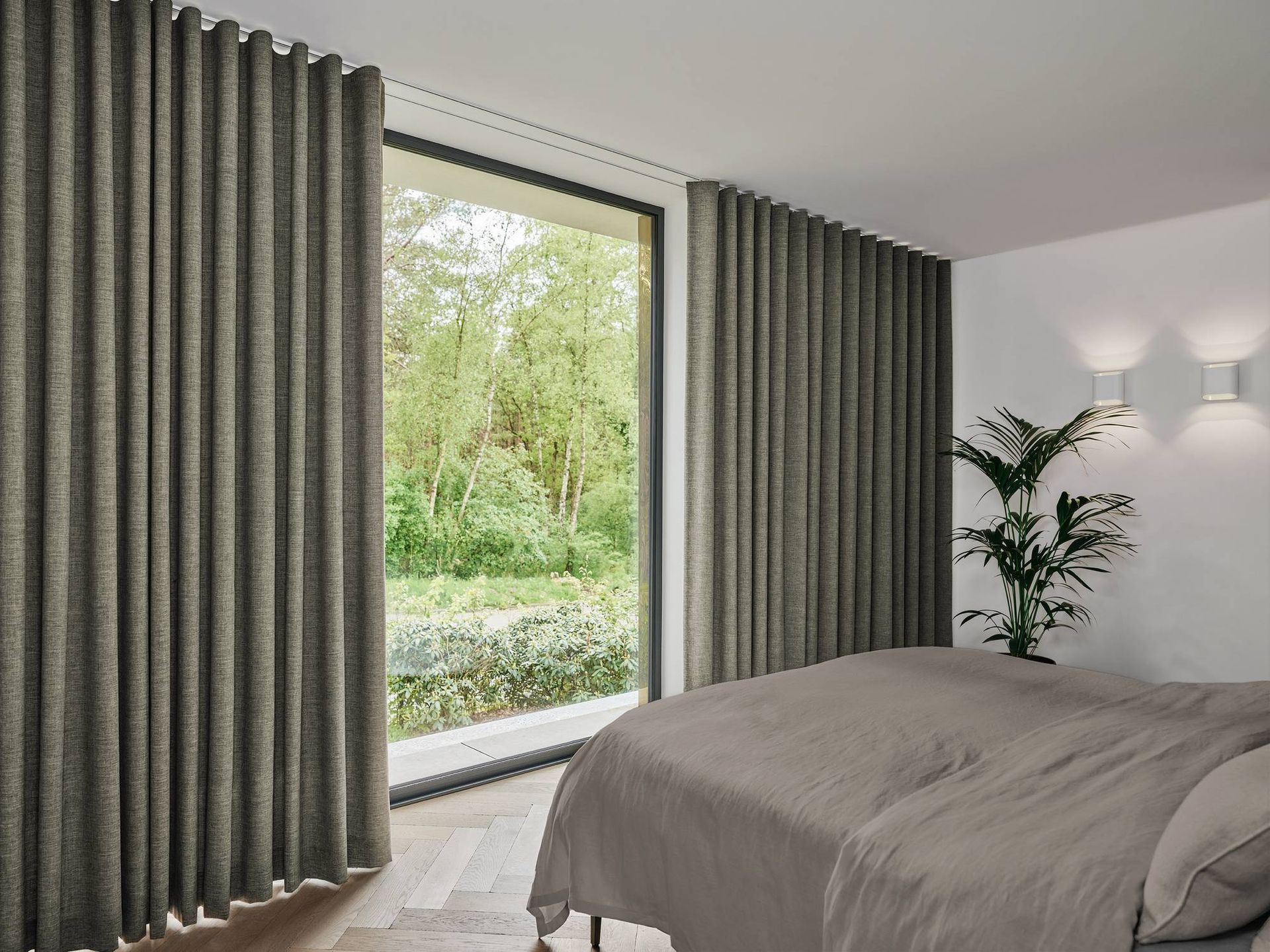 Moderne slaapkamer met een bed, een groot raam, grijze gordijnen en groen buiten te zien