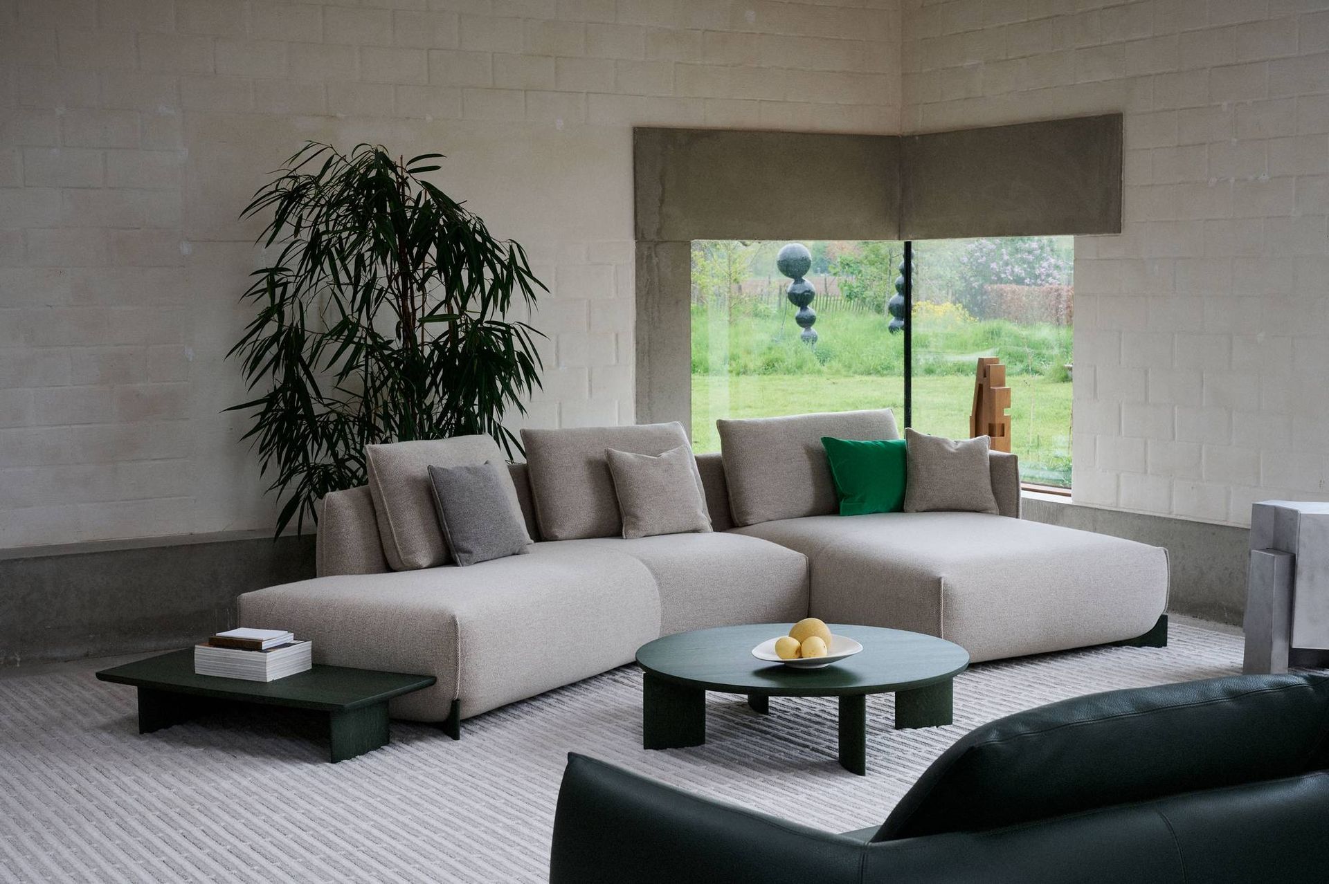 Moderne woonkamer met een beige hoekbank, groene salontafel, hoge plant en uitzicht vanuit een groot raam
