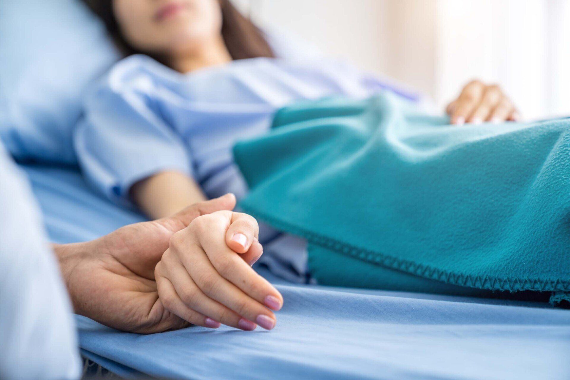 Person in hospital bed with hand held by another person.
