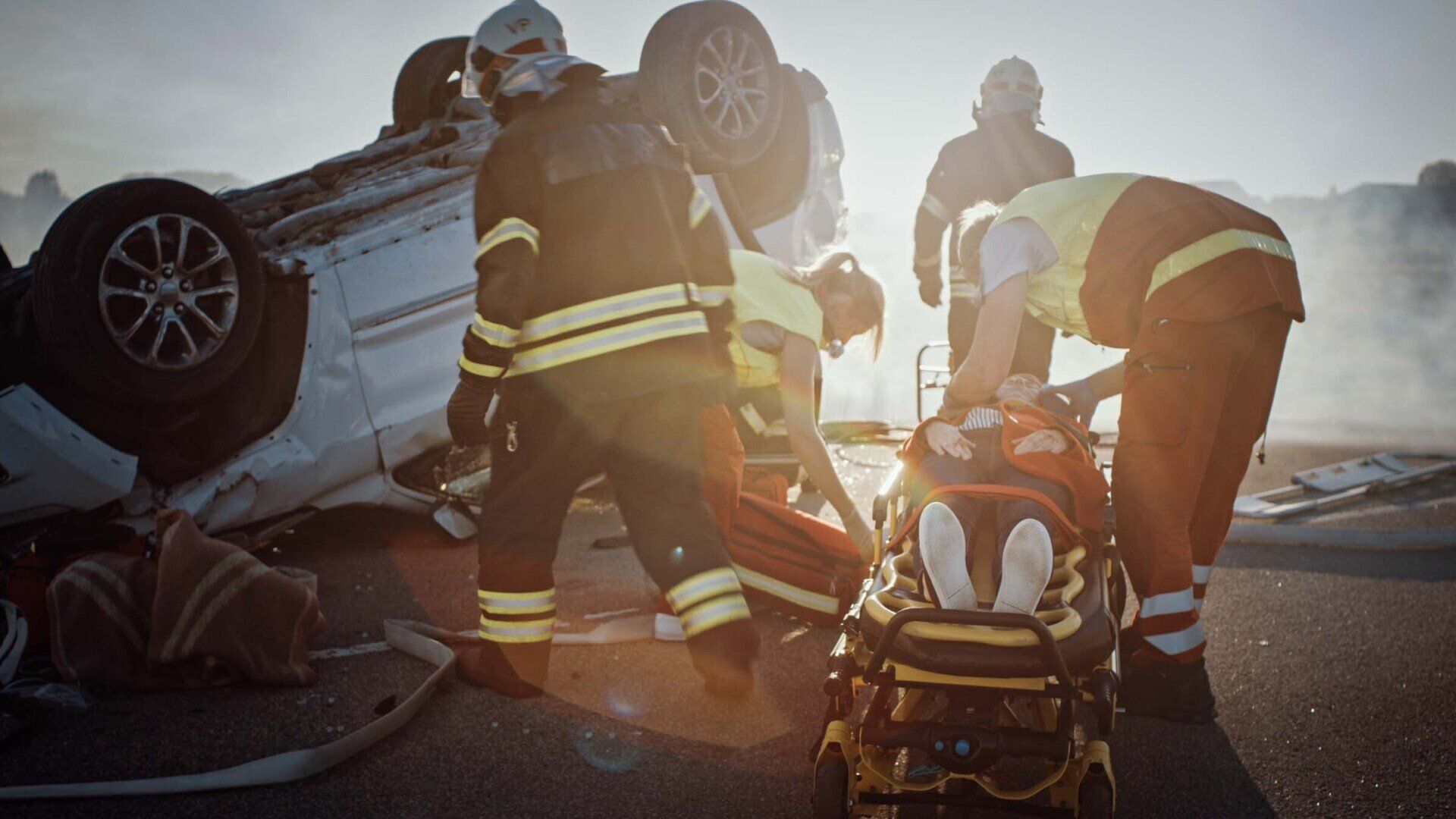 Emergency responders tending to accident victims near an overturned car on a road.