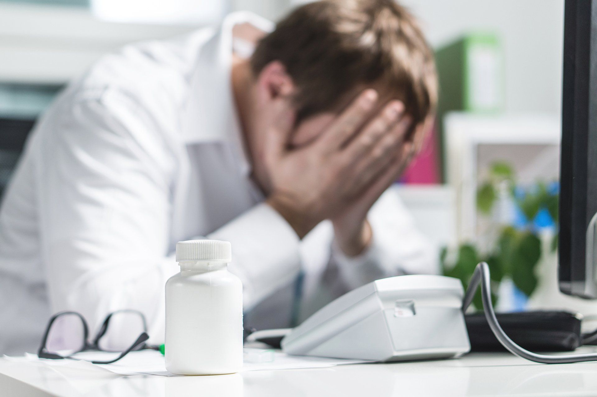 Stressed Doctor Cover Face Under Pressure - Detroit, MI - Frederic M Rosen, PC Attorney At Law Man in lab coat with head in hands, pills on desk.