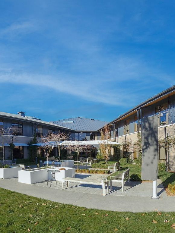 Courtyard with white benches, planters, and a building under a blue sky.