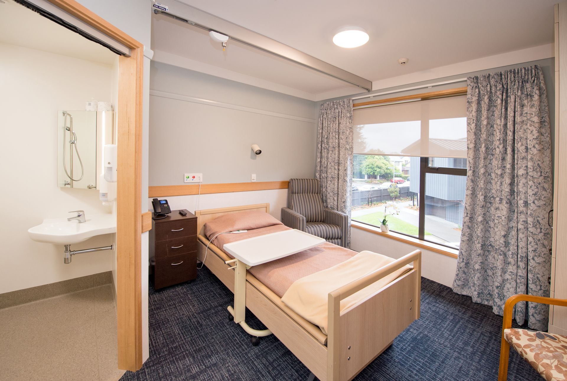 Bedroom in a care facility, with a bed, small side table, and open bathroom door.
