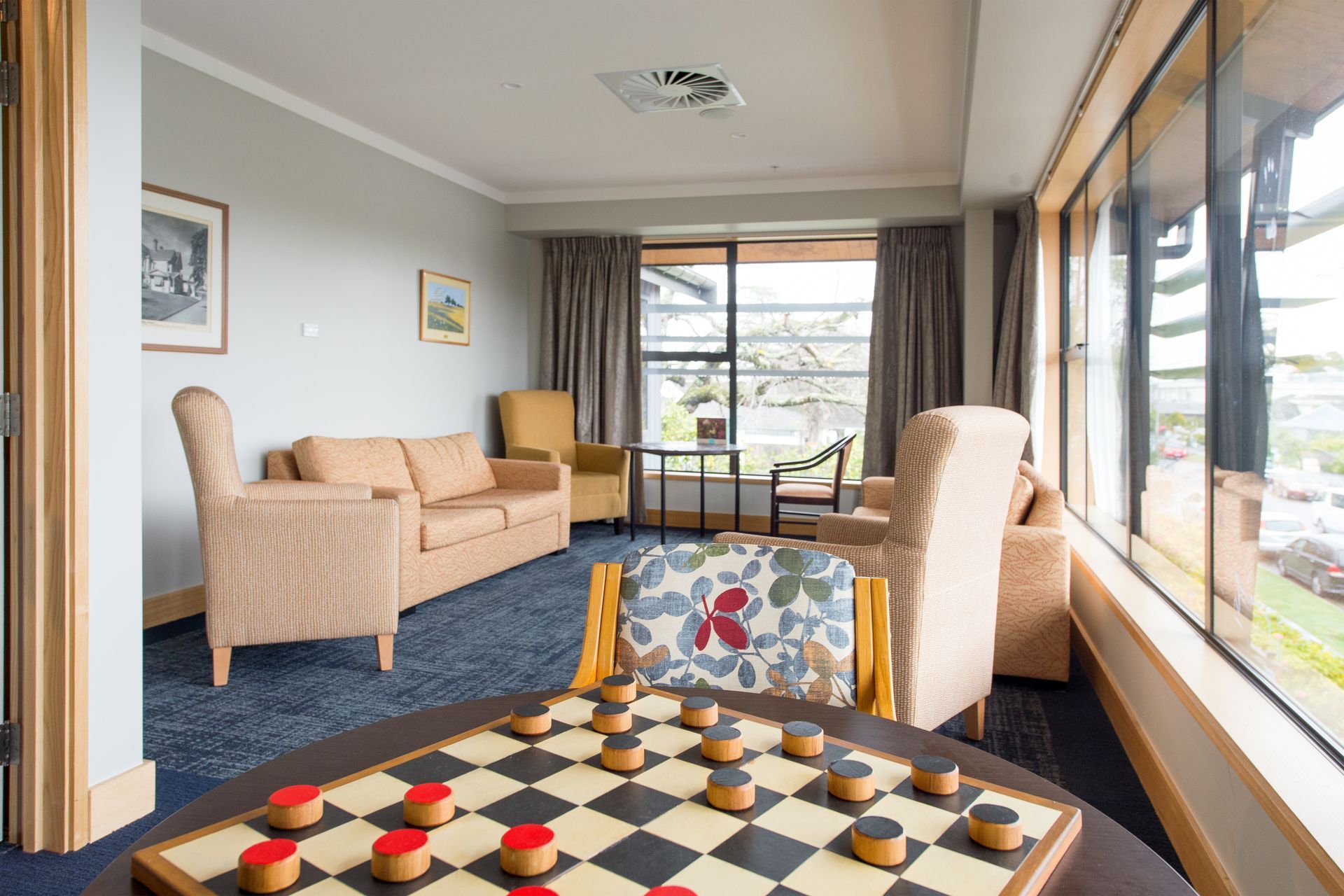 A room with a checkers board in the foreground, couches, and a window overlooking a garden.