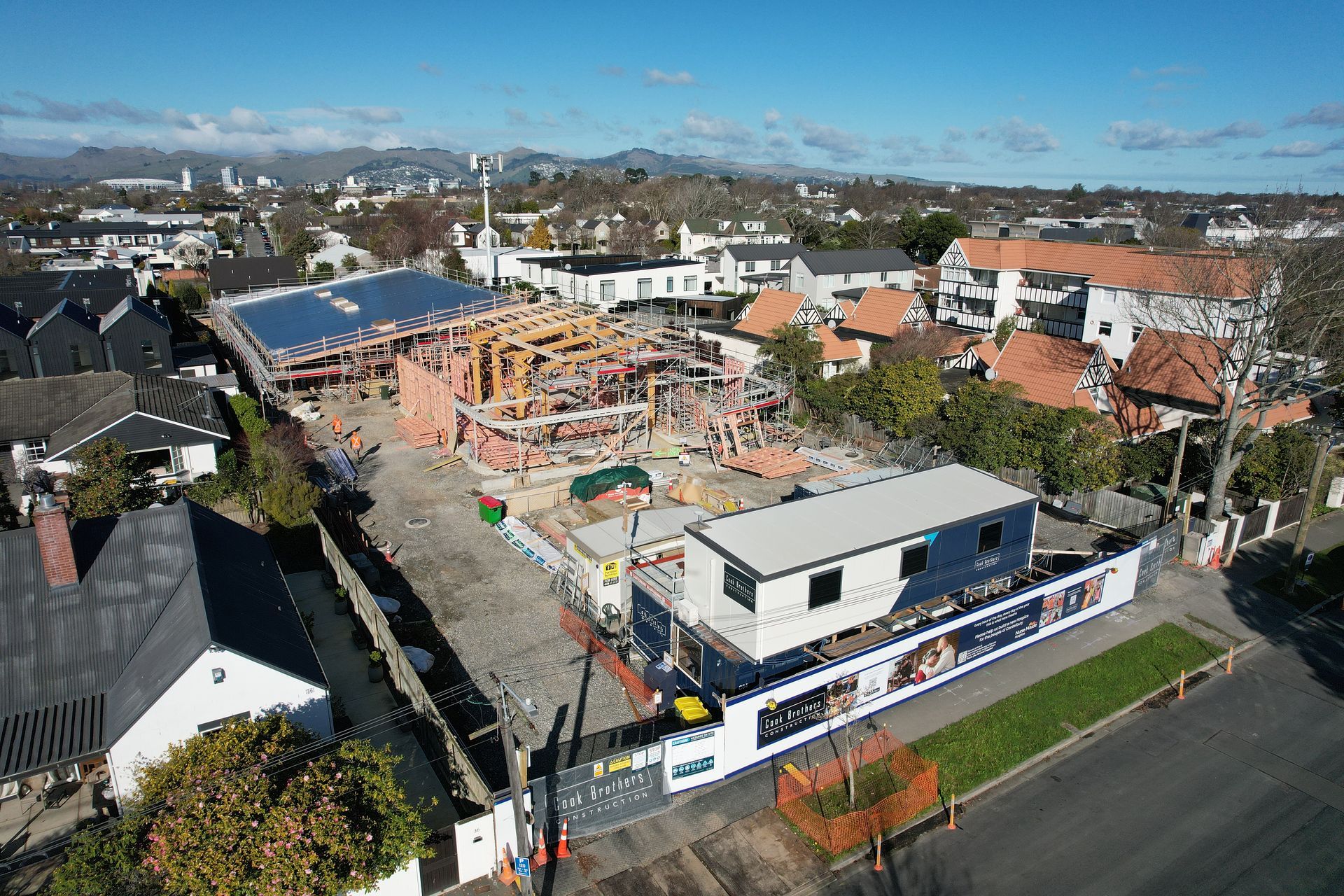 Construction site with wooden framework, surrounded by buildings and a container office.