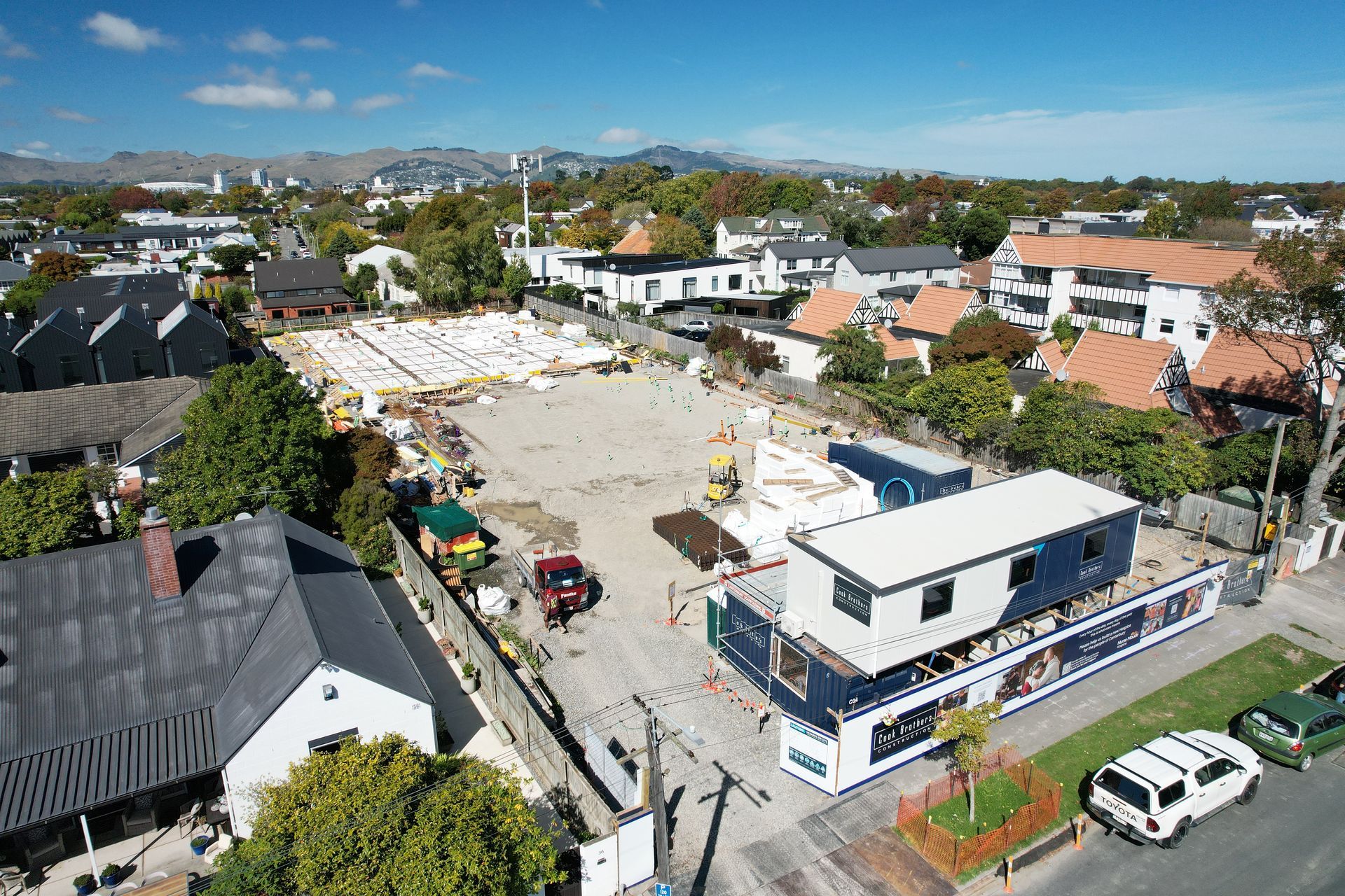 Construction site with shipping containers, debris, and surrounding houses.