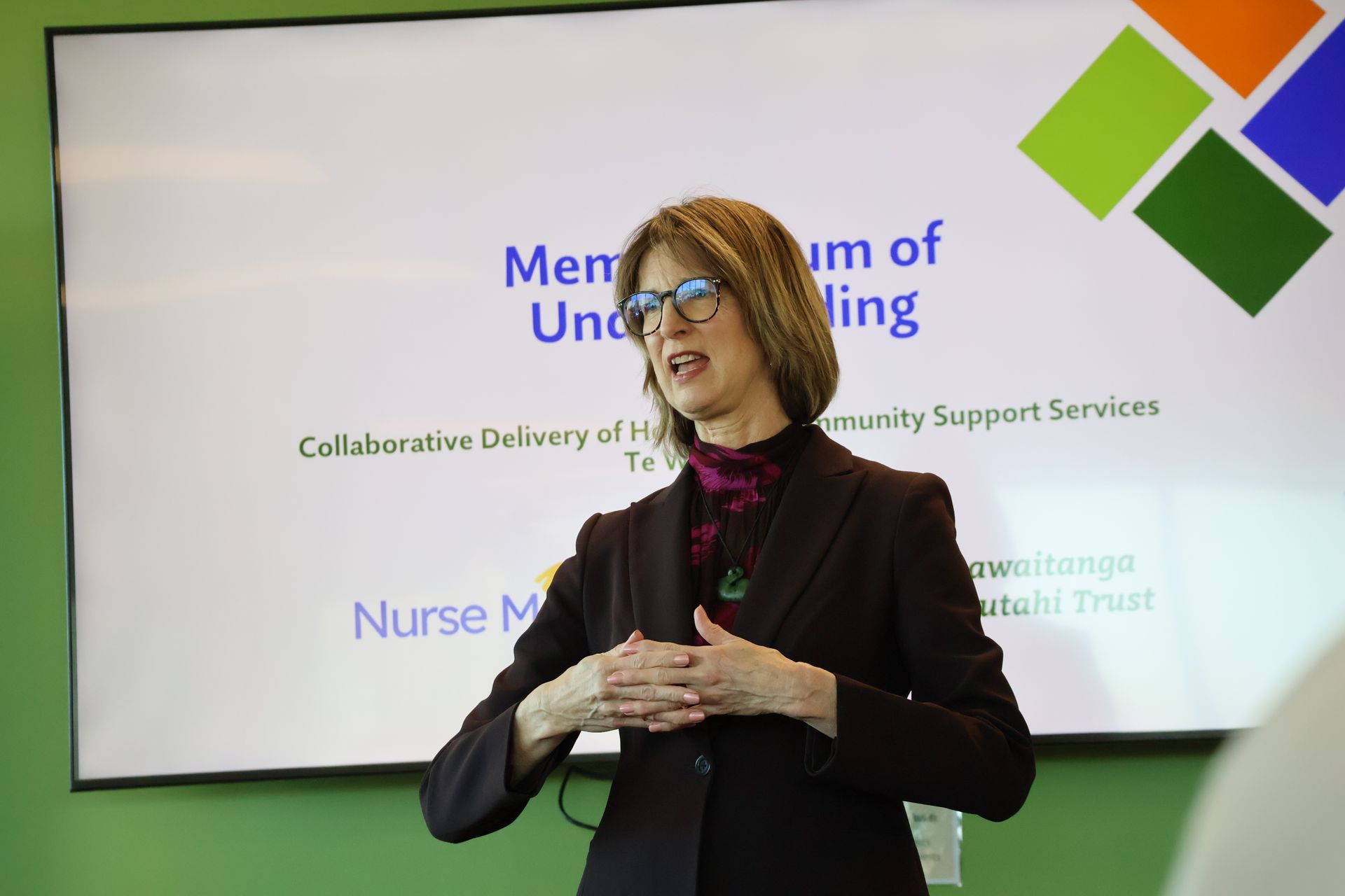 Woman speaking in front of presentation screen with colorful square logo.