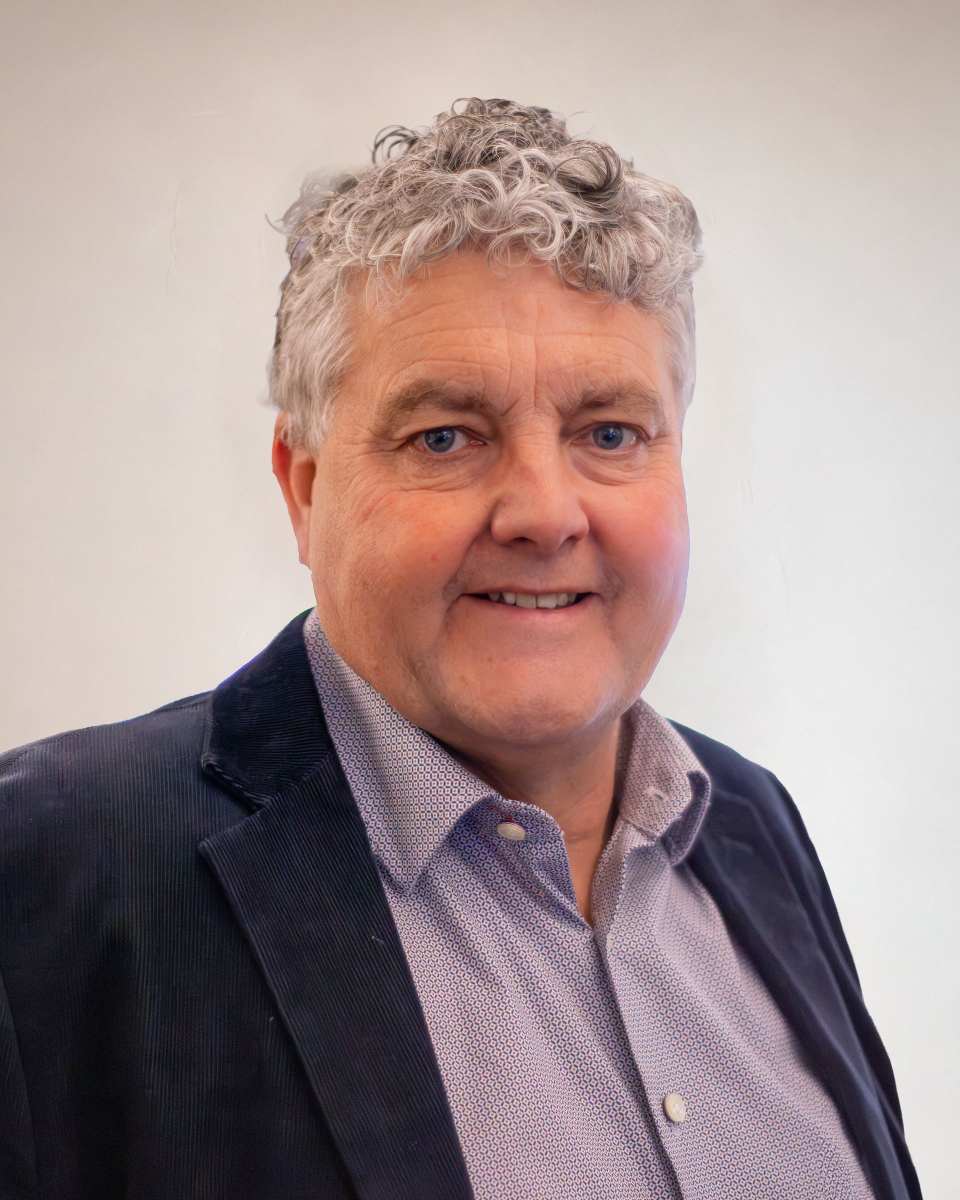 Portrait of a smiling person in a dark blazer and patterned shirt against a light background