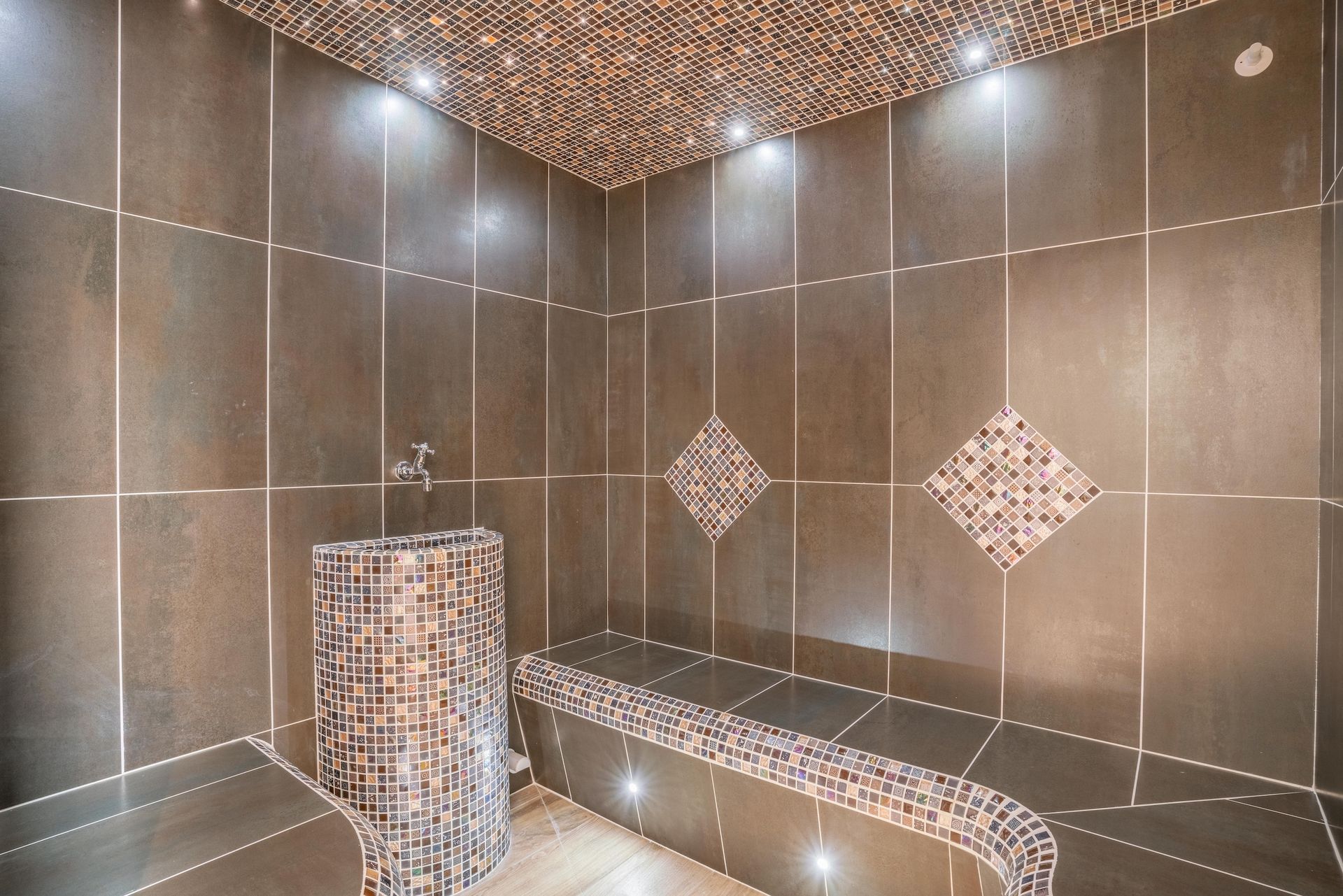 Hammam carrelé de noir avec banquettes et accents de mosaïque.