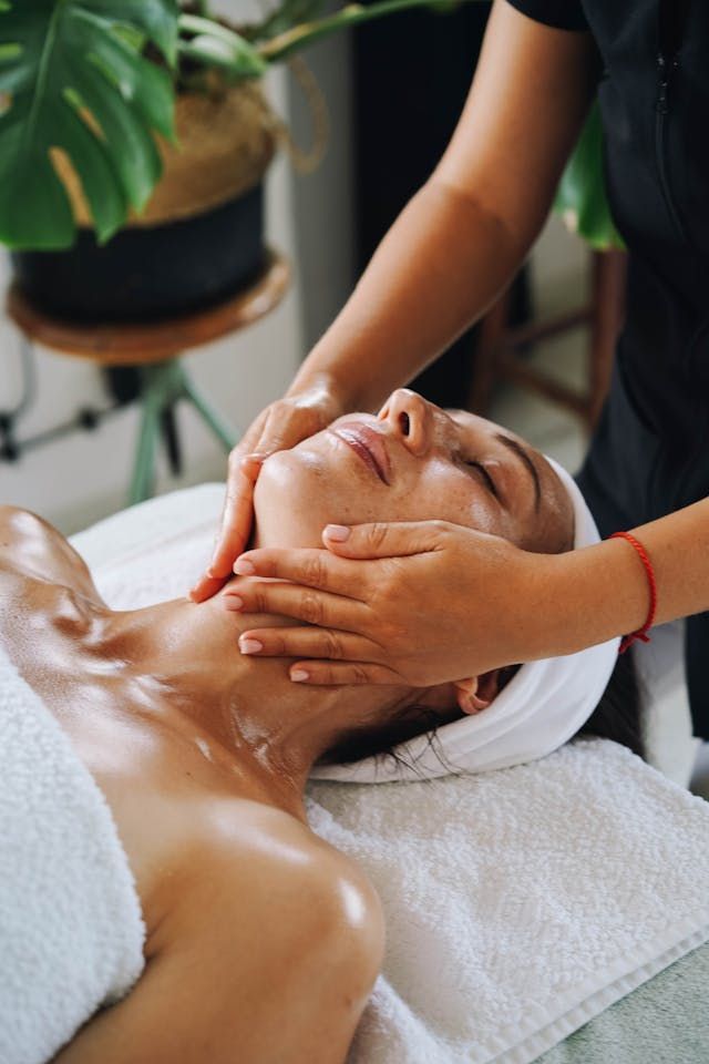 Personne recevant un massage facial dans un spa ; les mains du thérapeute sur le visage et le cou.