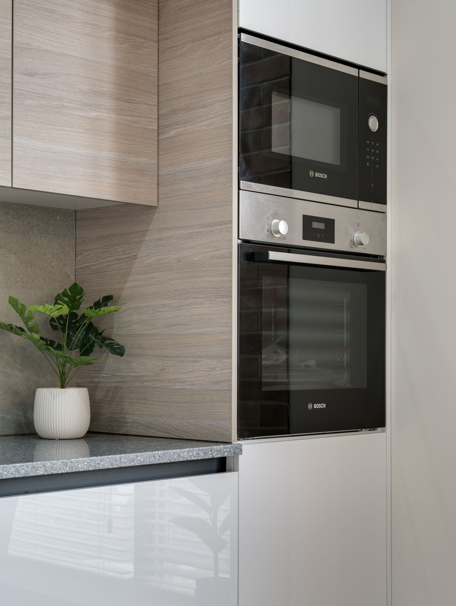 Modern kitchen with white cabinets, built-in oven and microwave, and a small plant on the counter