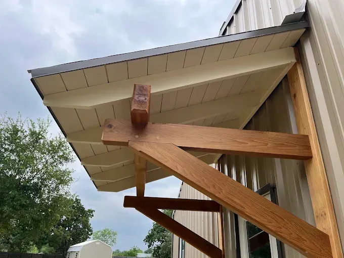 Wooden roof support braces under a beige house eave against a cloudy sky