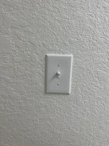 White light switch on a textured beige wall.