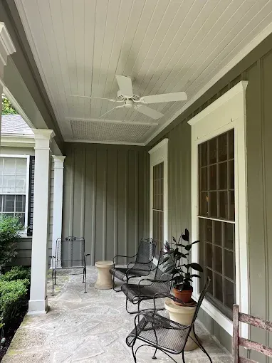 Covered front porch with white ceiling fan, wicker chairs, potted plant, and French doors.