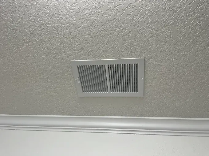 White ceiling vent above crown molding on a textured ceiling
