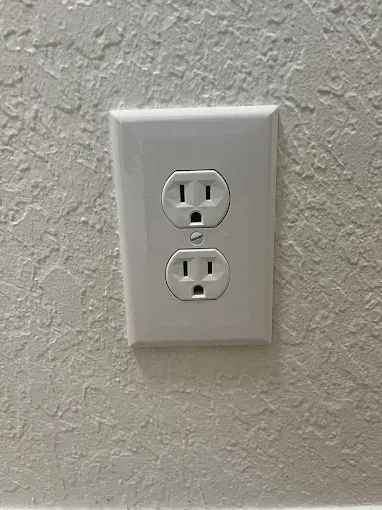 White wall outlet with two sockets and a switch plate on textured beige wall