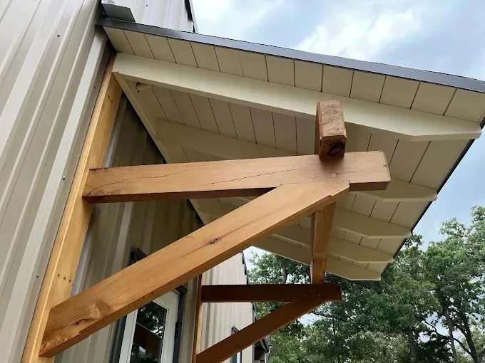 Wooden support braces under a house eave with white siding and a roof overhang