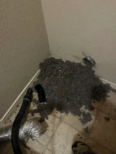 Gray debris and a damaged hose in a dirty corner on a tiled floor.