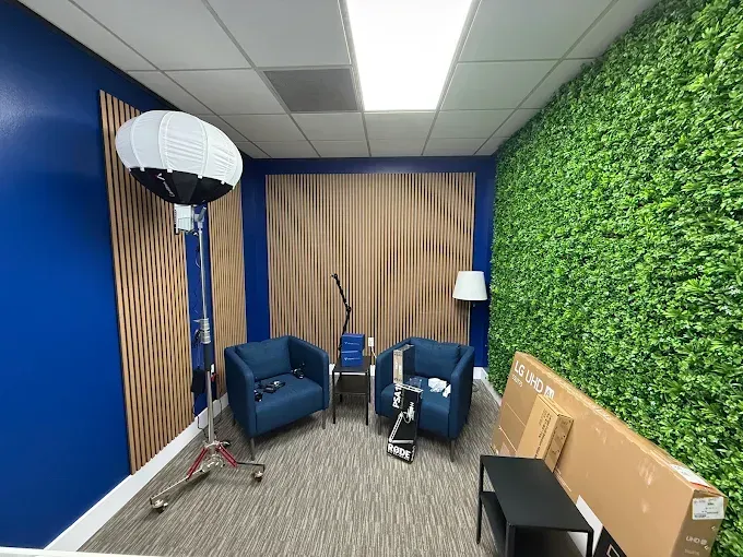Small office lounge with blue chairs, floor lamp, white floor lamp, wood slat wall, and green plant wall.