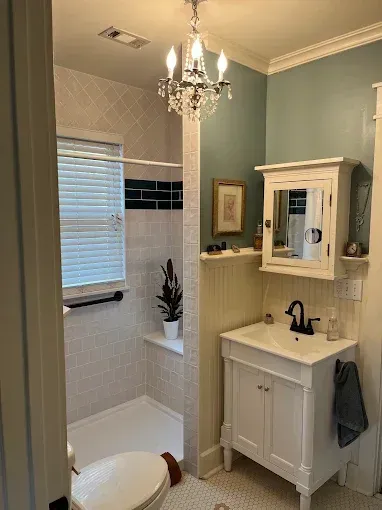 Small bathroom with white vanity, chandelier, pedestal mirror cabinet, and tiled shower.