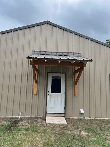 Small beige metal building with a white door and wooden awning under a cloudy sky