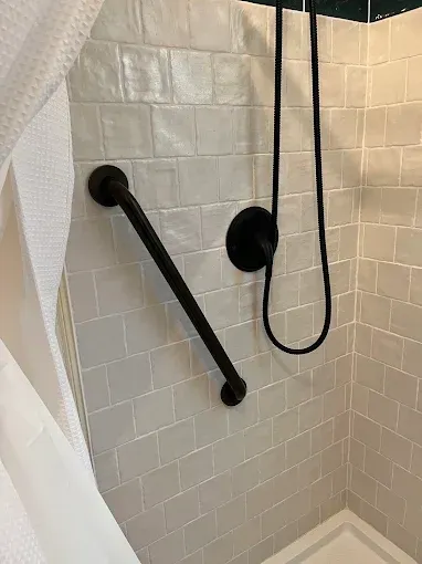 Accessible shower with black grab bar and handheld showerhead against white tile walls