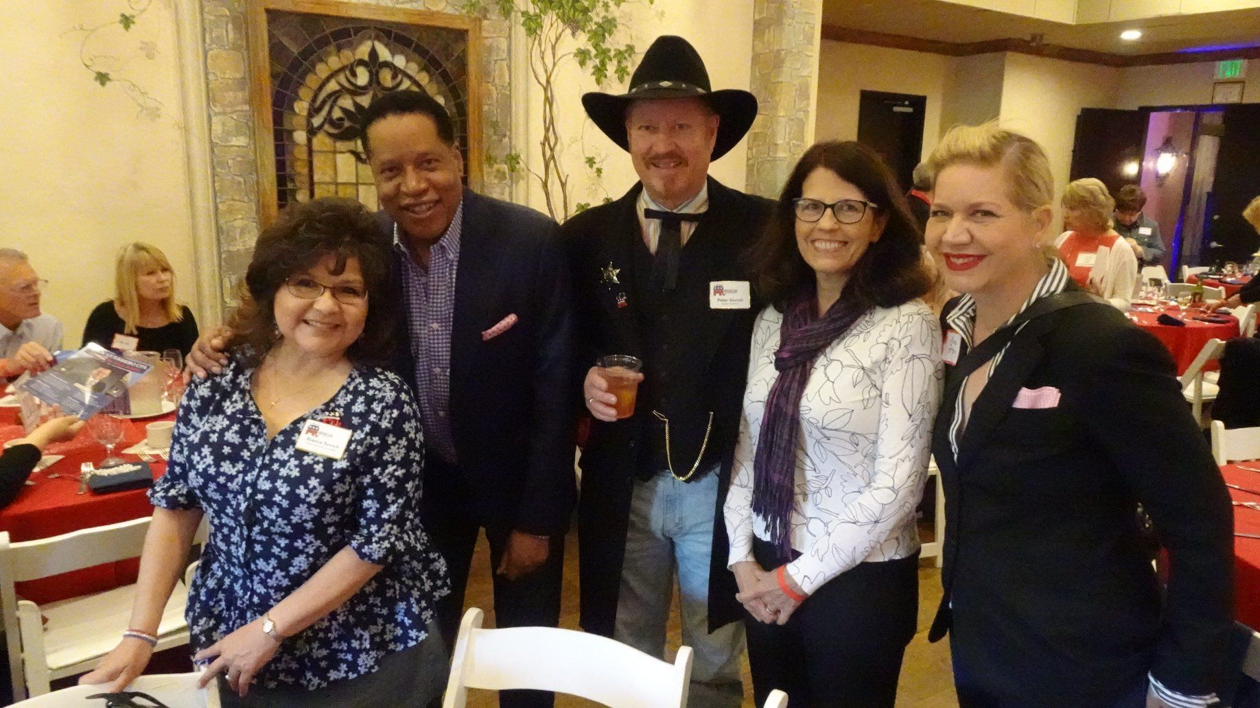 Group of five people smiling, posing for a photo at an event. A man in cowboy attire stands in the center.