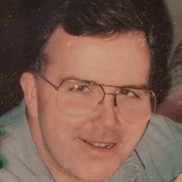 A man wearing glasses and a blue shirt is smiling for the camera.