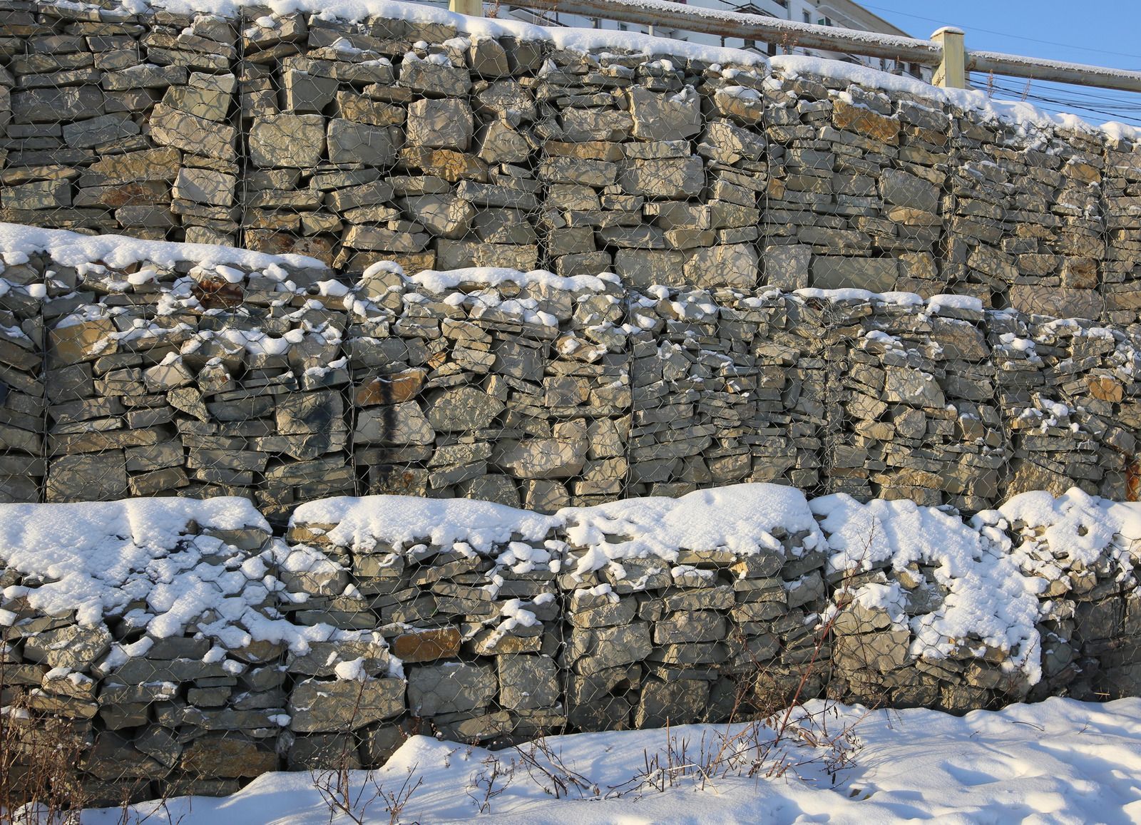 A stone wall covered in snow with a fence in the background
