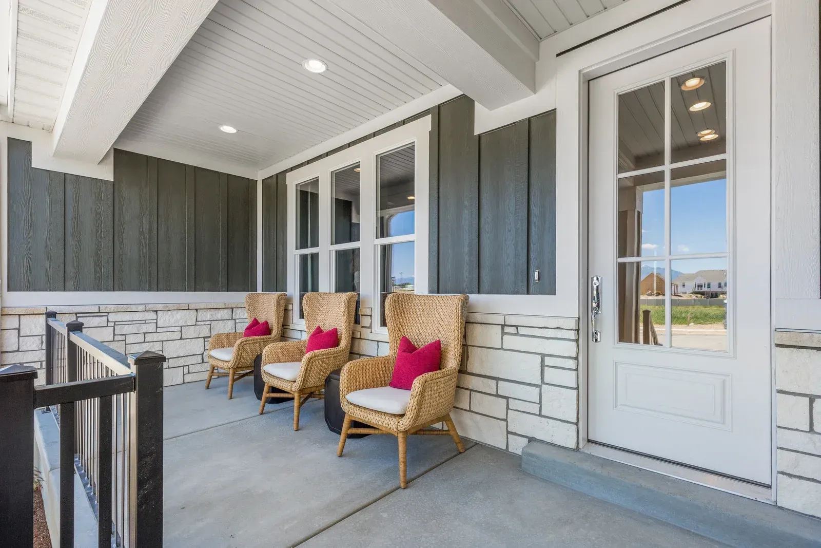 There are three chairs on the porch of a house.