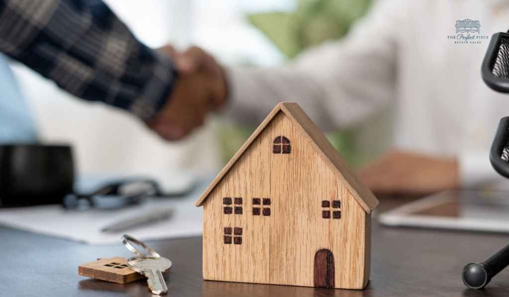 A man and woman shaking hands next to a model house and keys.