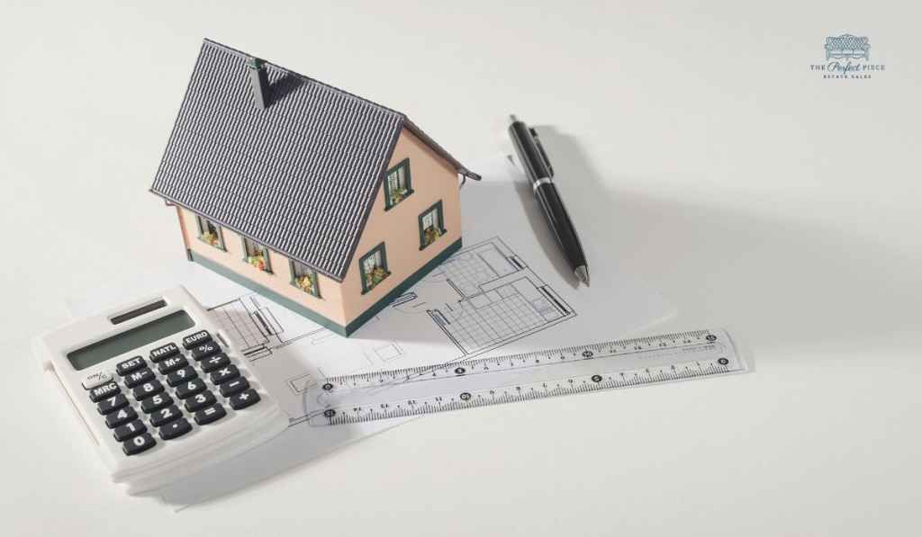 A model house is sitting on top of a calculator next to a ruler and pen.