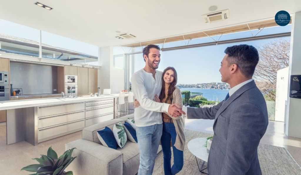 A man and woman are shaking hands with a real estate agent in a living room.
