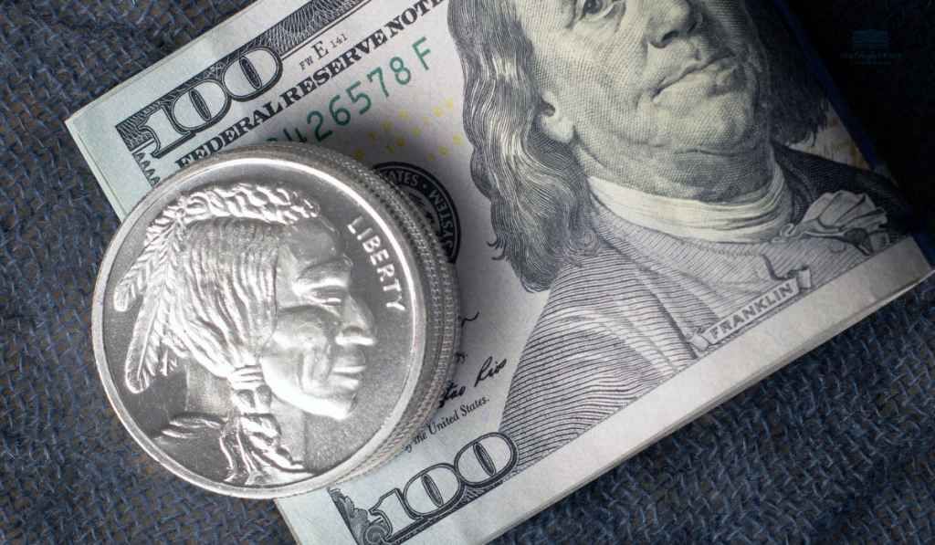 A silver coin is sitting on top of a 100 dollar bill.