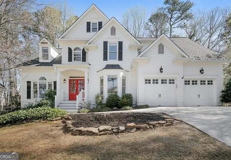 White house with black shutters, red front door, and three-car garage. Brown landscaping in front.